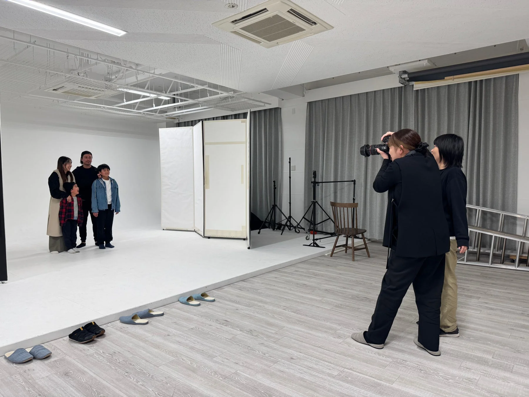 カメラマンが白い背景の前でポーズをとる家族を撮影