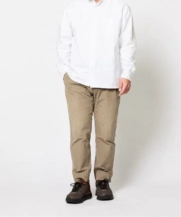 白い長袖シャツとベージュのパンツ、暗い色のスニーカーを着用した男性