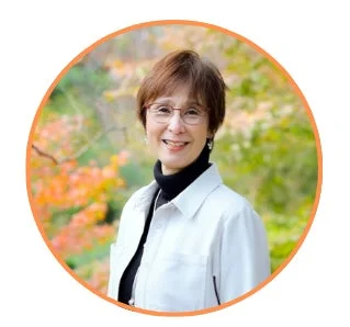 笑顔でカメラを見つめる眼鏡をかけた中高年の女性のポートレートです。