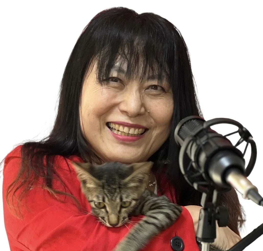 赤い服を着た笑顔のアジア人女性が子猫を抱き、隣にはマイクが写っています。ポッドキャストや配信をしているような和やかな雰囲気です。