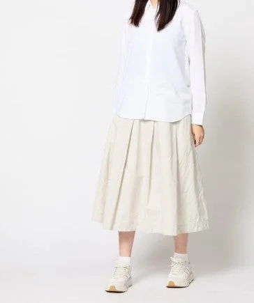 白い長袖シャツとライトベージュのプリーツミモレ丈スカートを着用した女性
