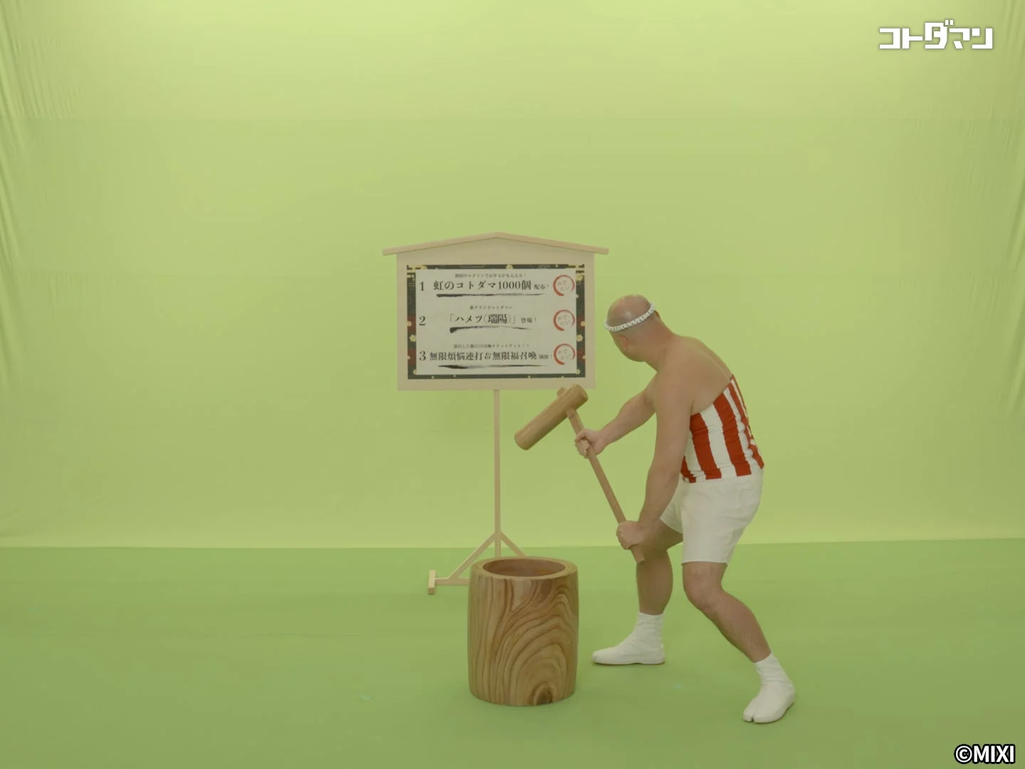 鉢巻と赤白の縞模様の衣装を着た男性が、大きな木製の杵と臼で餅つきをしている様子