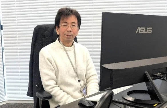 オフィスで白いセーターを着てカメラに向かって微笑むアジア人男性