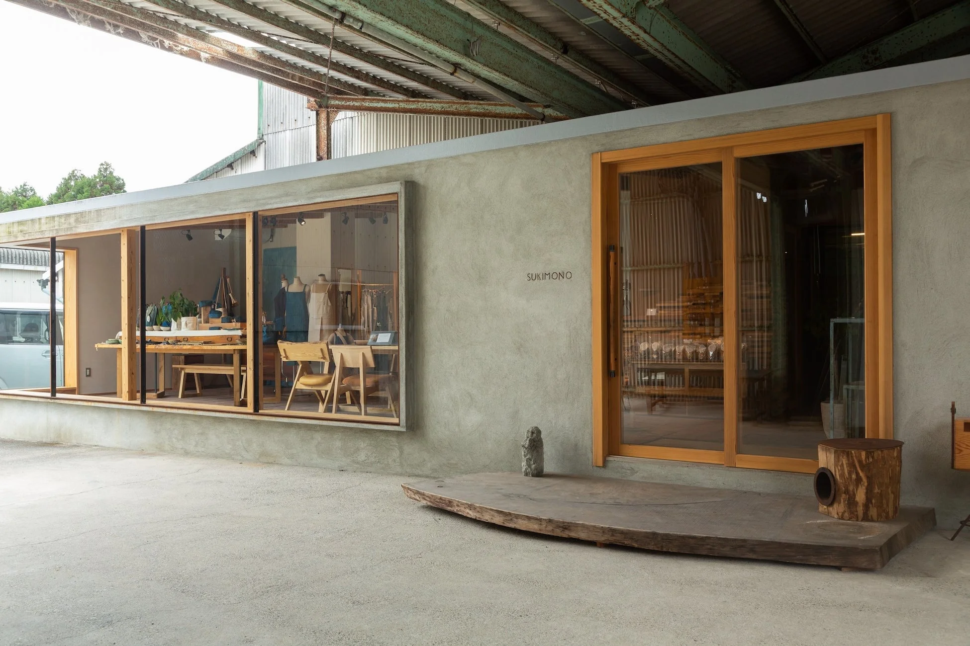 コンクリートの壁に大きな木枠の窓とドアが特徴的な店舗の外観です。