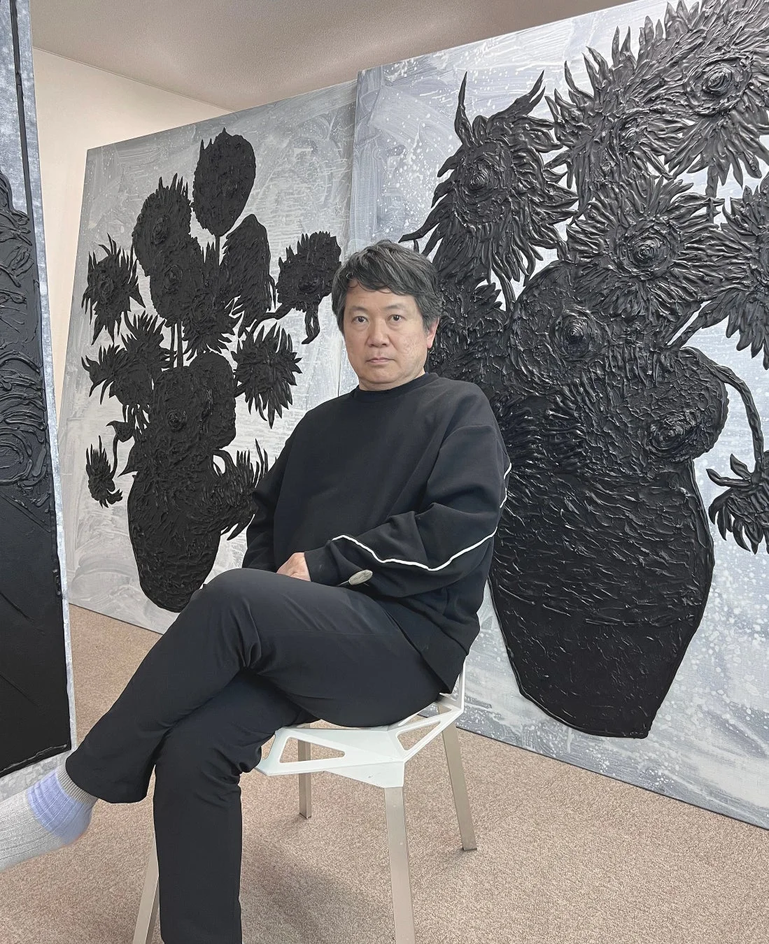 黒い服を着た男性とひまわりのような花瓶の絵画