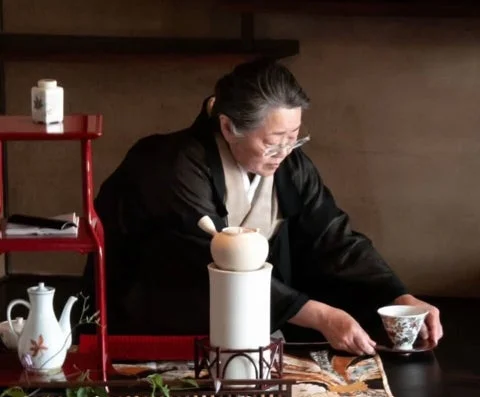 和服を着た女性が伝統的な茶器を使い、丁寧にお茶の準備をしている様子