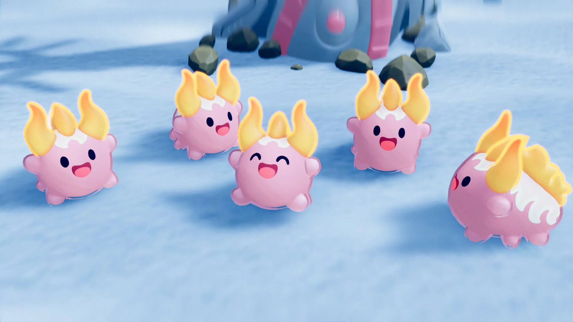 雪のような青白い地面に、ピンク色の可愛らしいクリーチャーが5匹集まっている様子。それぞれが笑顔で、頭には黄色い炎のような角が生えており、ゲームのワンシーンを思わせます。