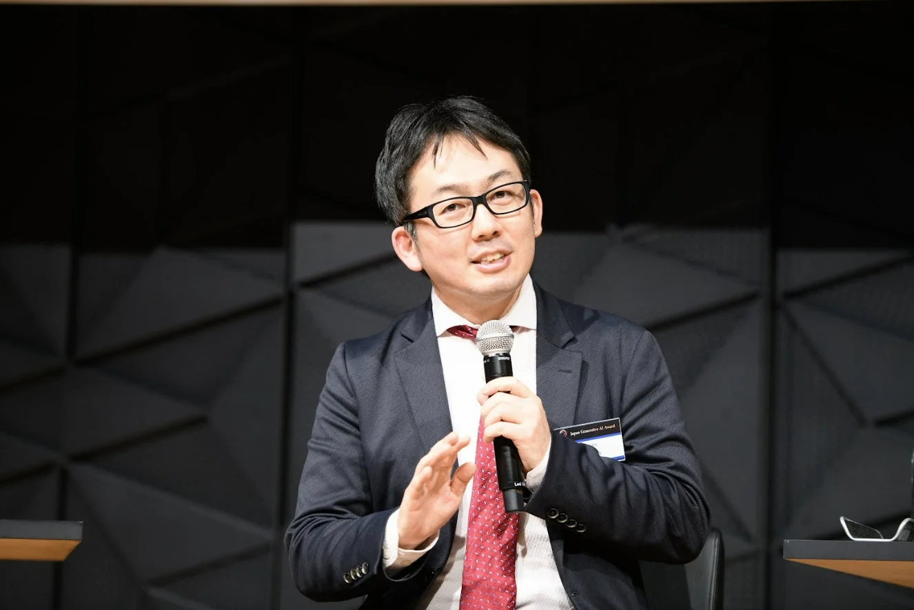 マイクを手に講演するスーツ姿の男性