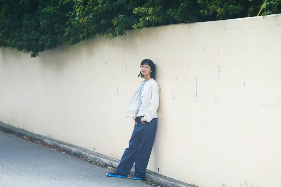 明るい色の壁に寄りかかり微笑む関ゆうか氏