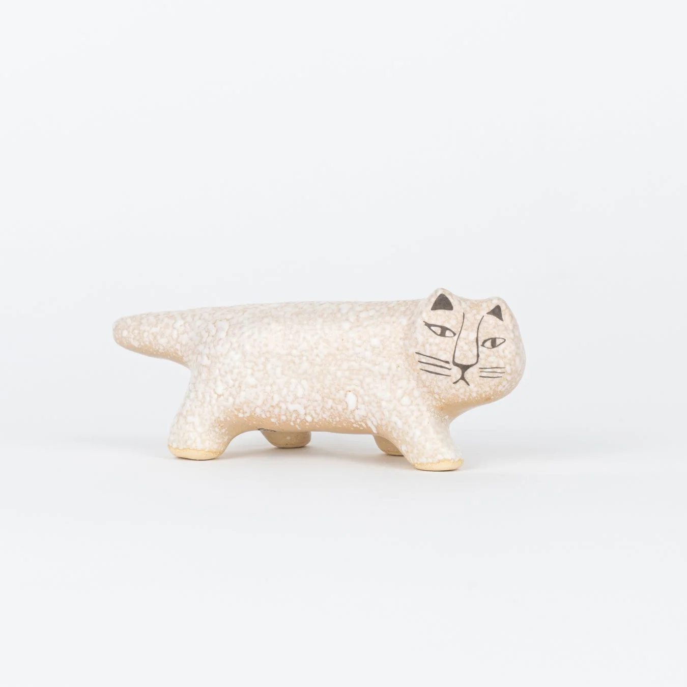 白い背景に、ざらつきのある質感のベージュ色の陶器の猫の置物が写っています。簡素化された顔立ちが特徴で、かわいらしい雰囲気を醸し出しています。