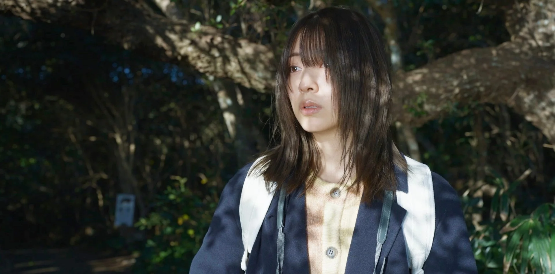 木漏れ日が差す森の中、憂鬱そうな表情の女性