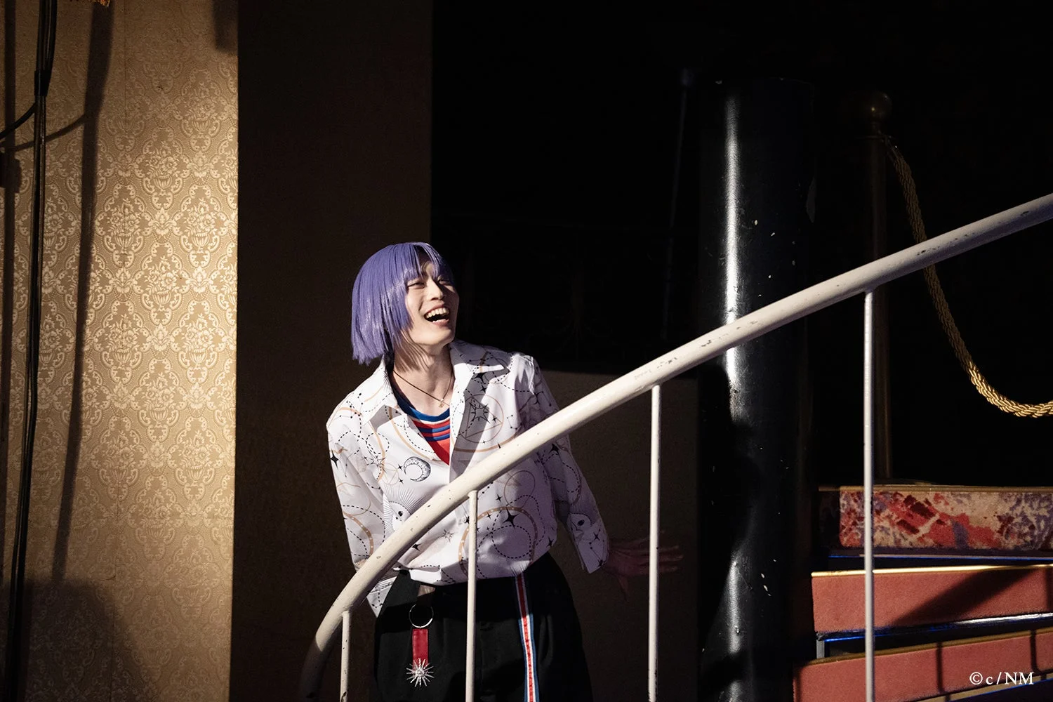 笑顔で階段のそばに立つ魔法使い役のキャスト