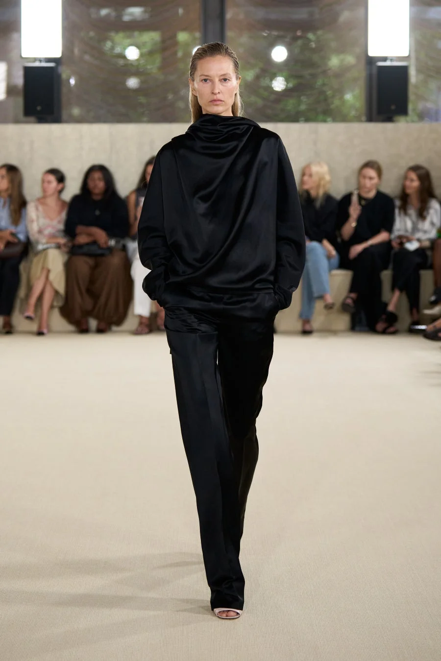 黒い光沢のあるサテンのトップスとパンツを着用したモデル