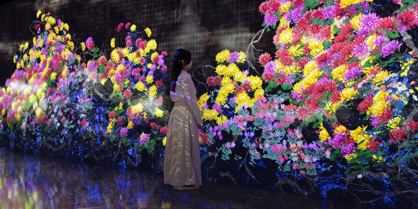女性が色鮮やかな菊のデジタルアートインスタレーションの前に立っています。