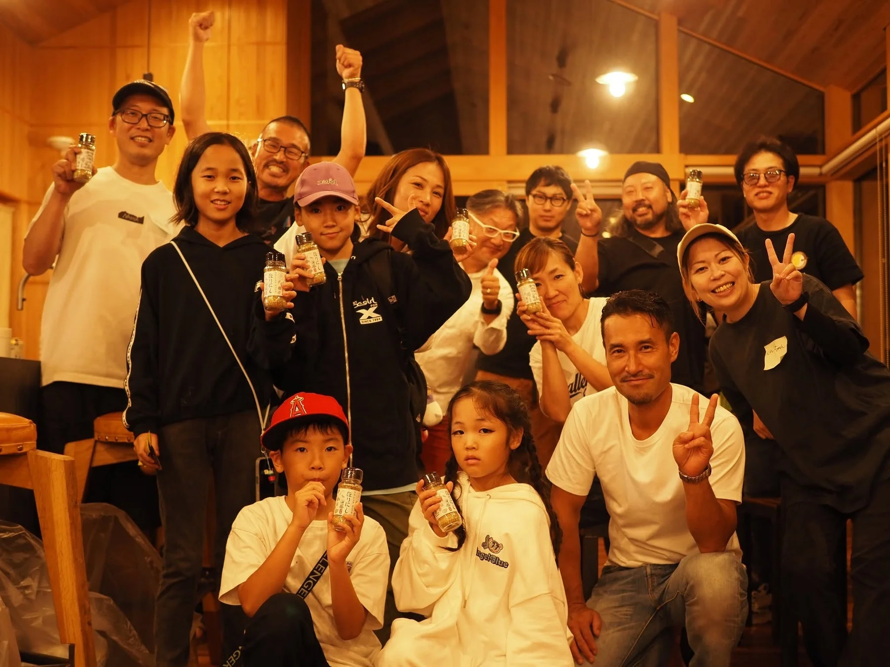 大人と子供を含む日本人グループが、手作りふりかけのボトルを持ち、笑顔でポーズをとっている集合写真。皆がピースサインや拳を上げており、和やかで楽しいイベントの雰囲気が伝わってきます。