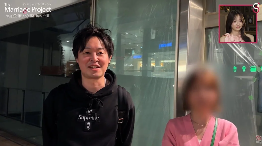 一人の男性がカメラに向かって話しており、その横には顔がぼかされた女性が立っている。左上には「The Marriage Project」のロゴがあり、右上には別の女性の顔が映る小窓がある。