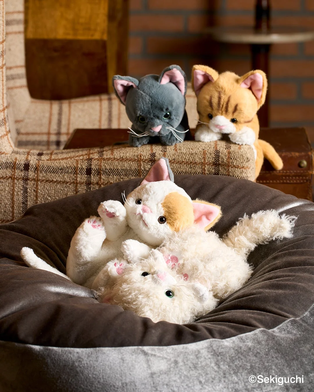 ソファとクッションの上でくつろぐ複数の猫のぬいぐるみ