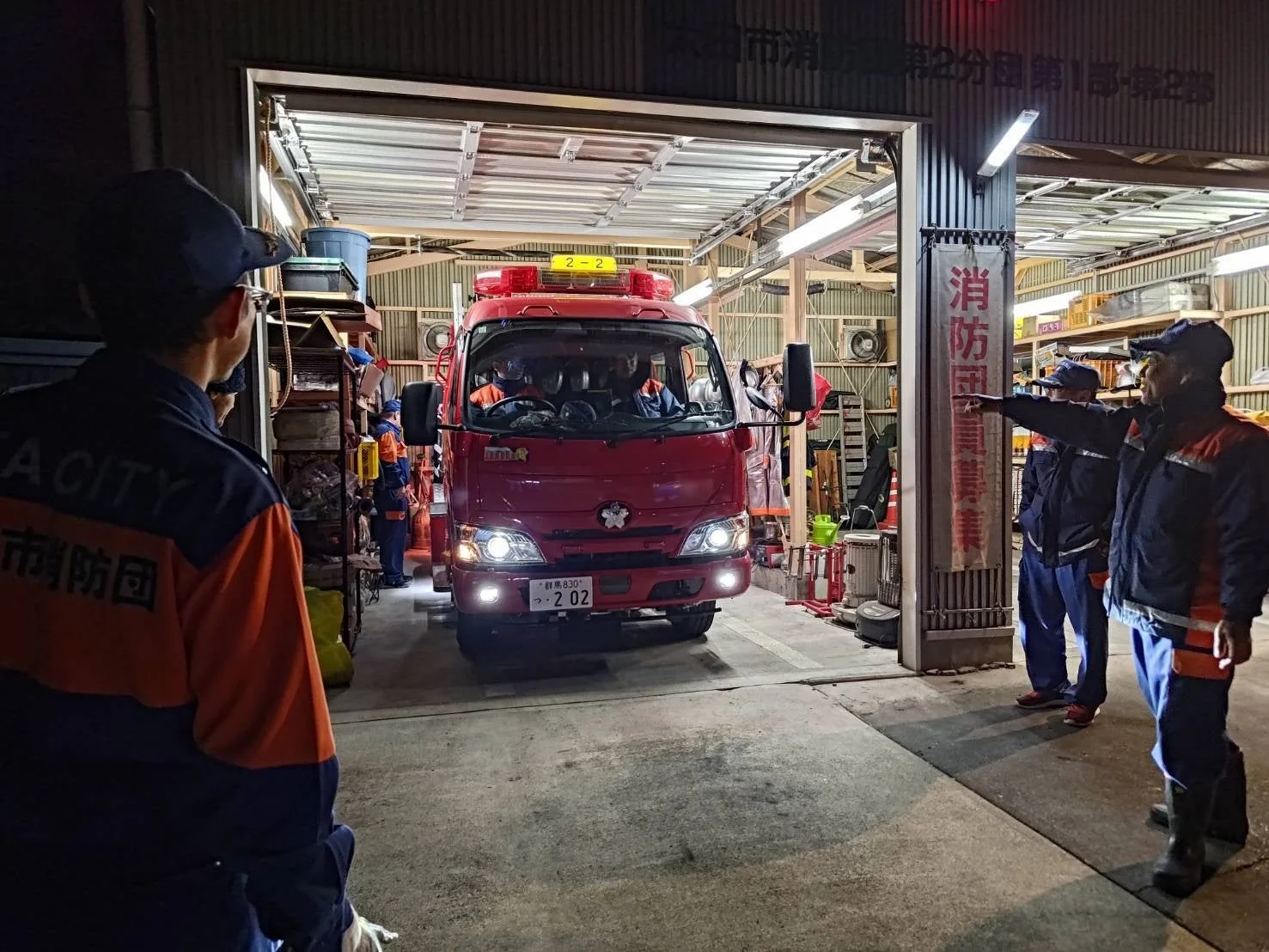 夜間、消防団のガレージから赤い消防車が出動しようとしている様子を捉えた画像です。