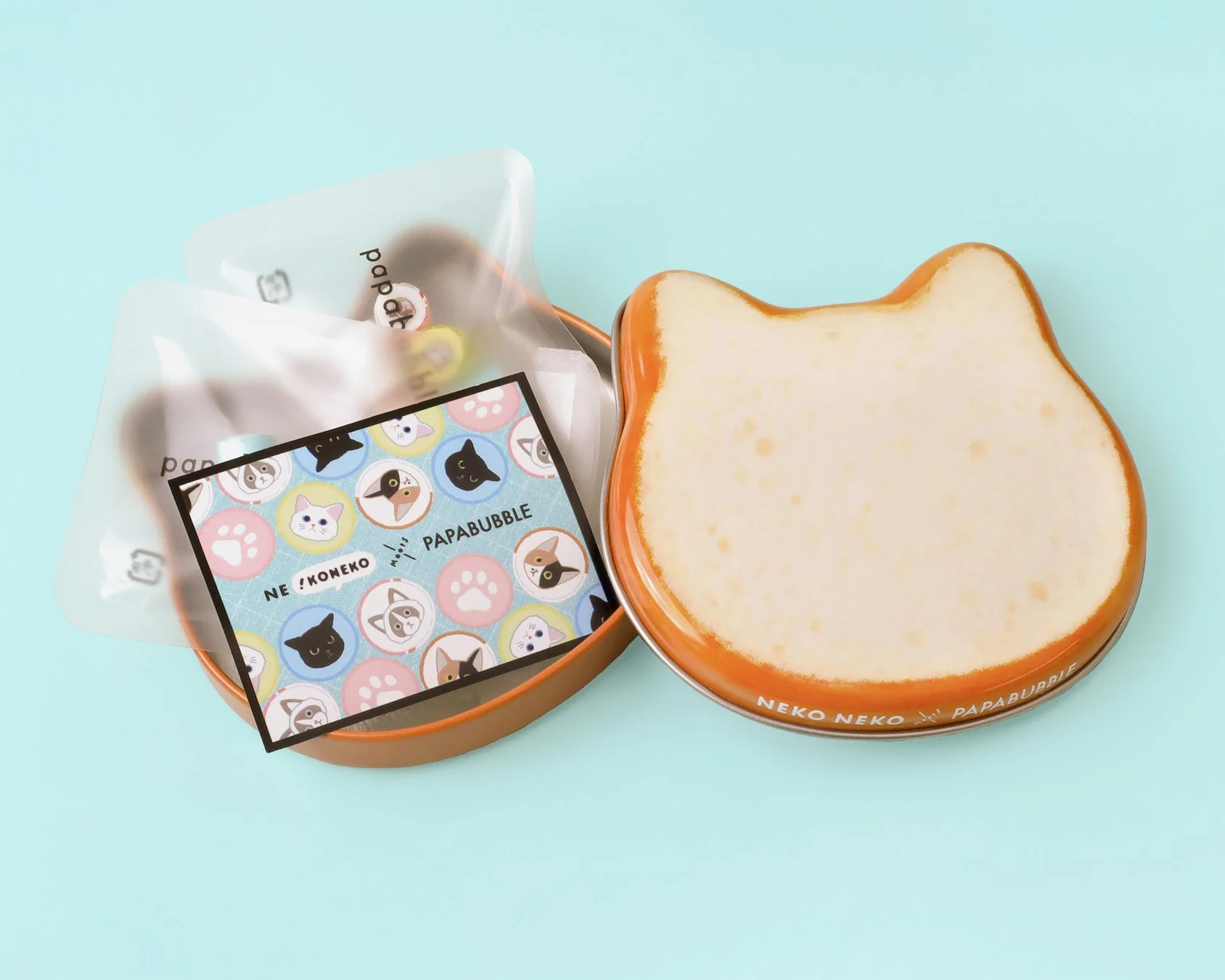 猫の形をした可愛らしい缶と、猫のイラストが描かれたカードや透明な袋に入ったお菓子が写っています。