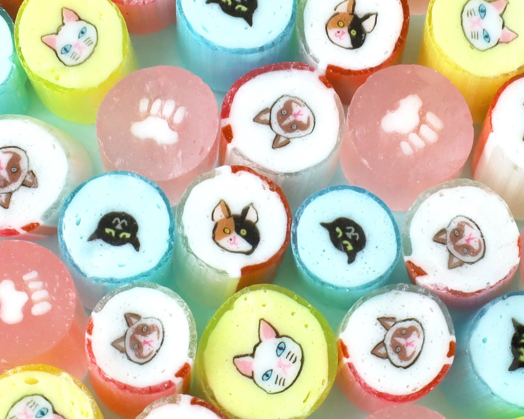 猫の顔や肉球の可愛らしいデザインが施された、様々な色合いのカラフルな飴が並べられているクローズアップ画像です。