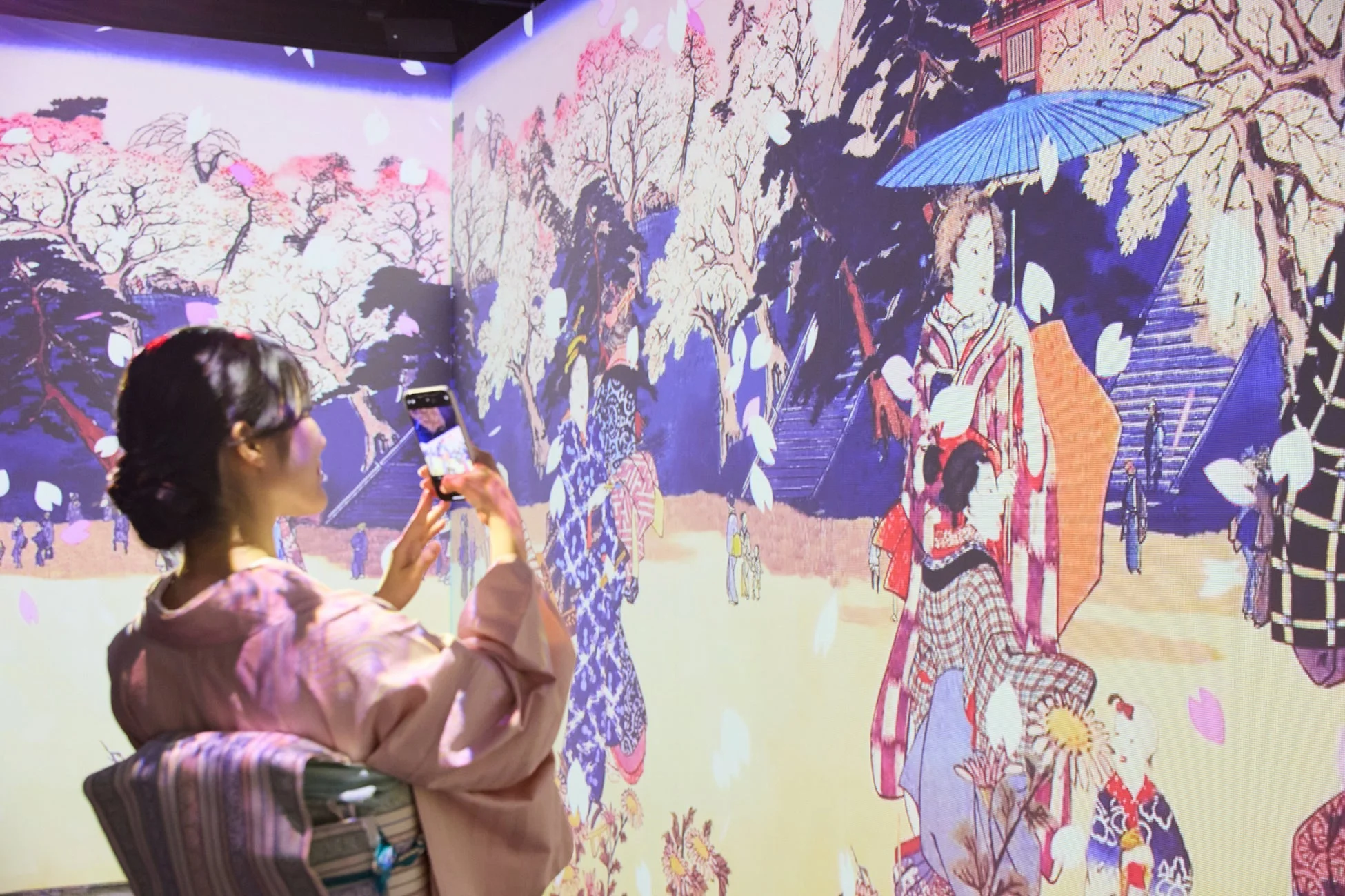 桜が舞い散るデジタルアートを撮影する来場者