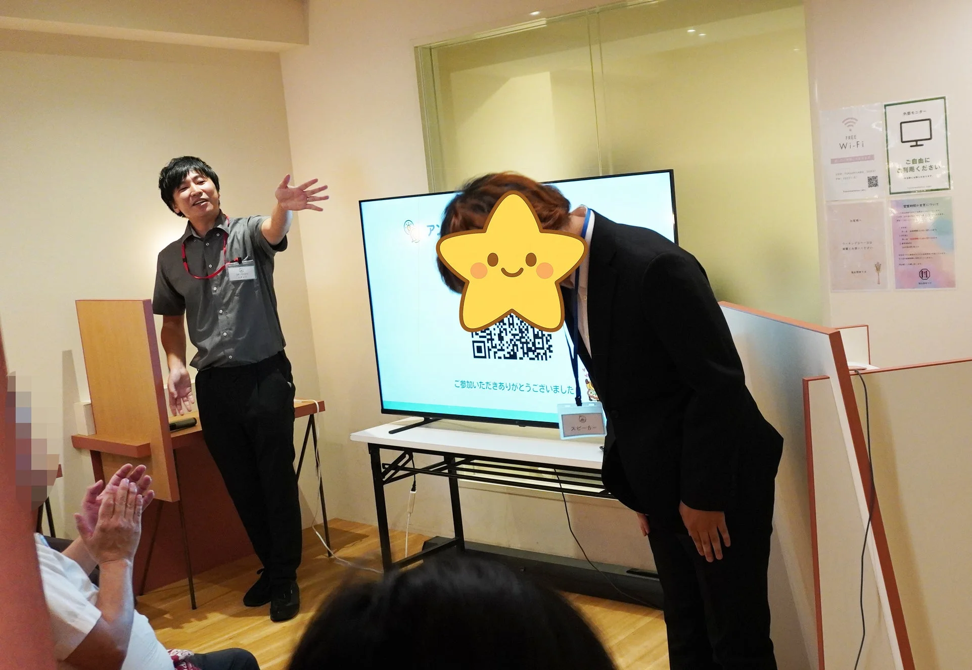 セミナー会場で、スピーカーが聴衆に感謝を述べ、別の一人がお辞儀をしている様子