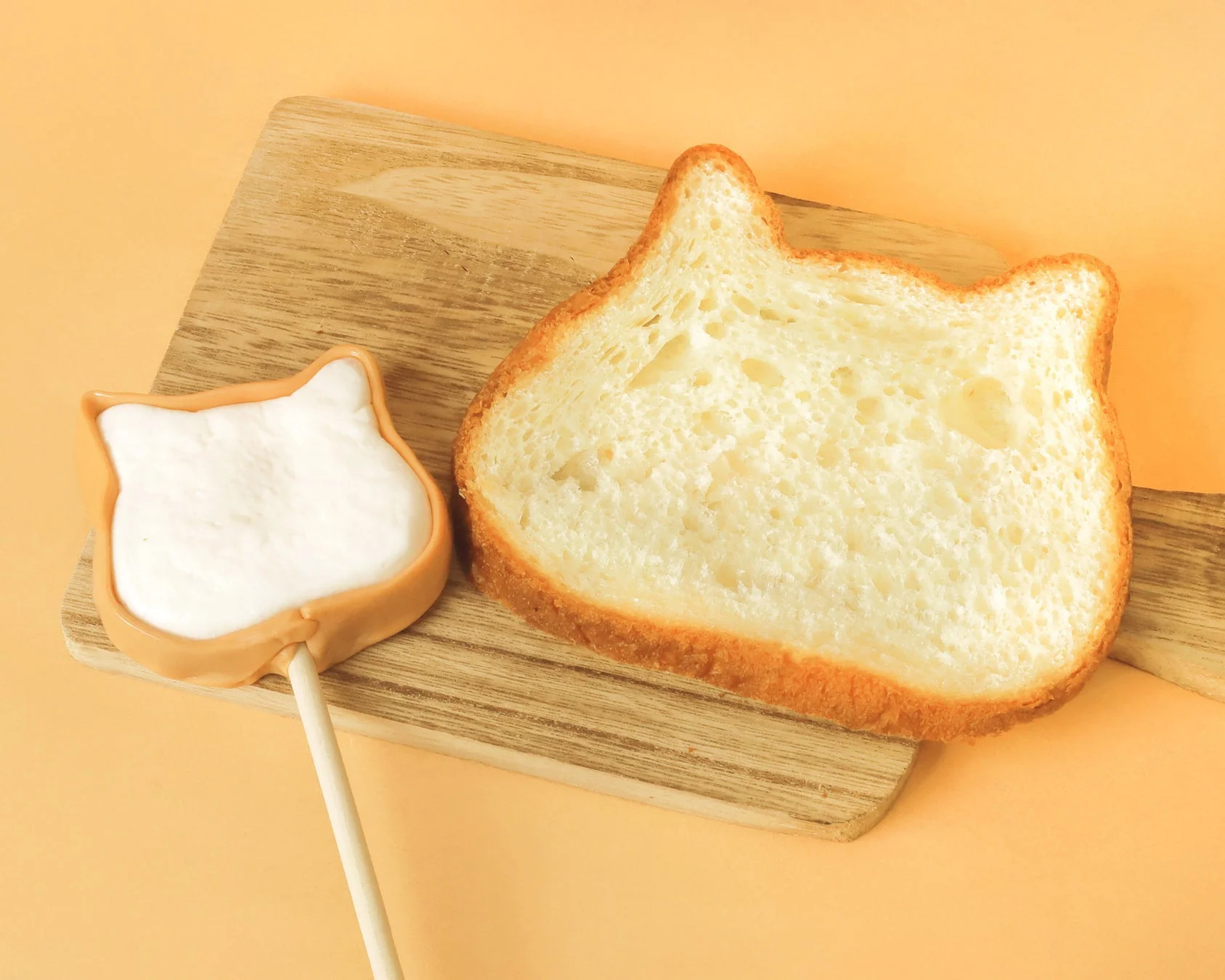 猫の形にカットされた食パンと、棒付きの猫型マシュマロが木製のまな板に置かれています。