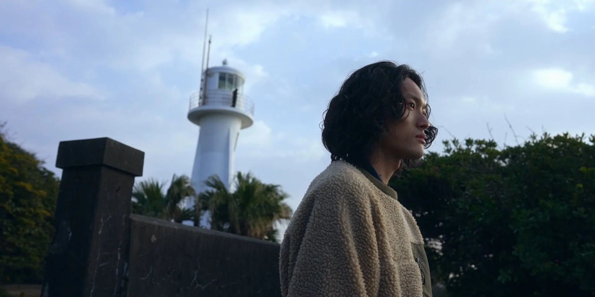 灯台を背景に遠くを見つめる男性