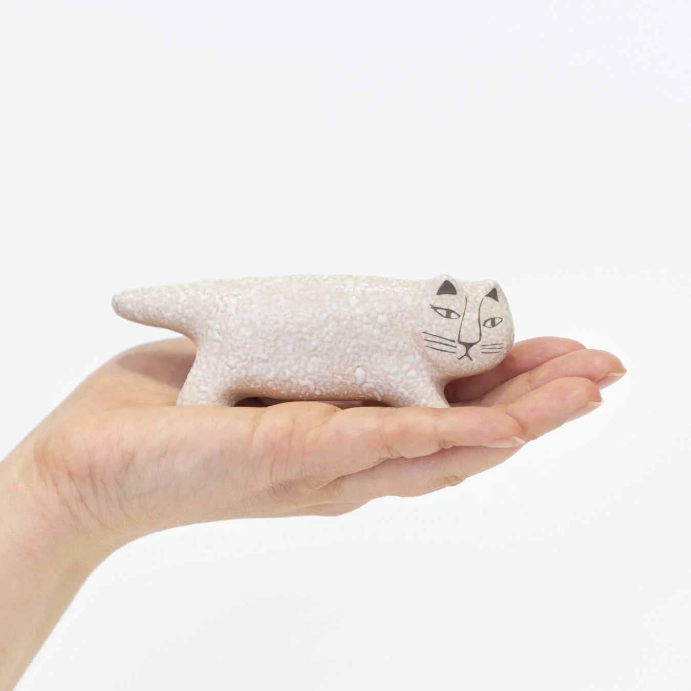 人の掌にのせられた、リサ・ラーソンデザインと思われる白い猫の陶器の置物です。独特の表情が特徴的で、可愛らしい雰囲気を醸し出しています。