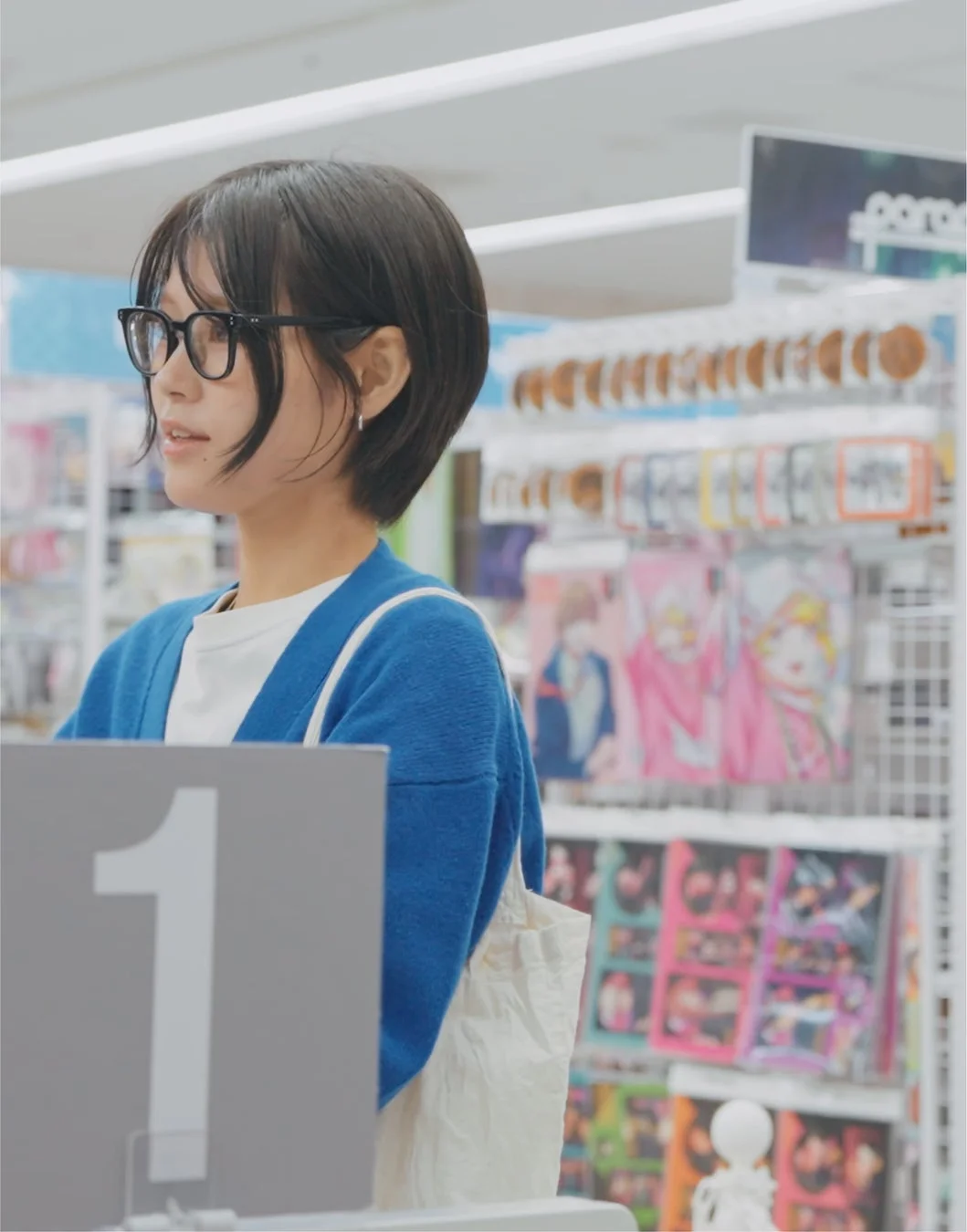 アニメや漫画のポスターが見える店内で、女性がカウンターに立っている様子