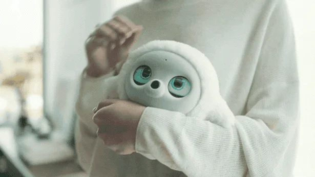 白いふわふわした愛らしいロボットを人が優しく抱きかかえている様子