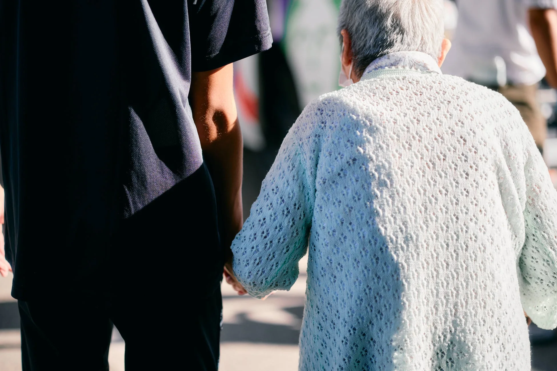 高齢者と若い人が手をつないで歩く後ろ姿