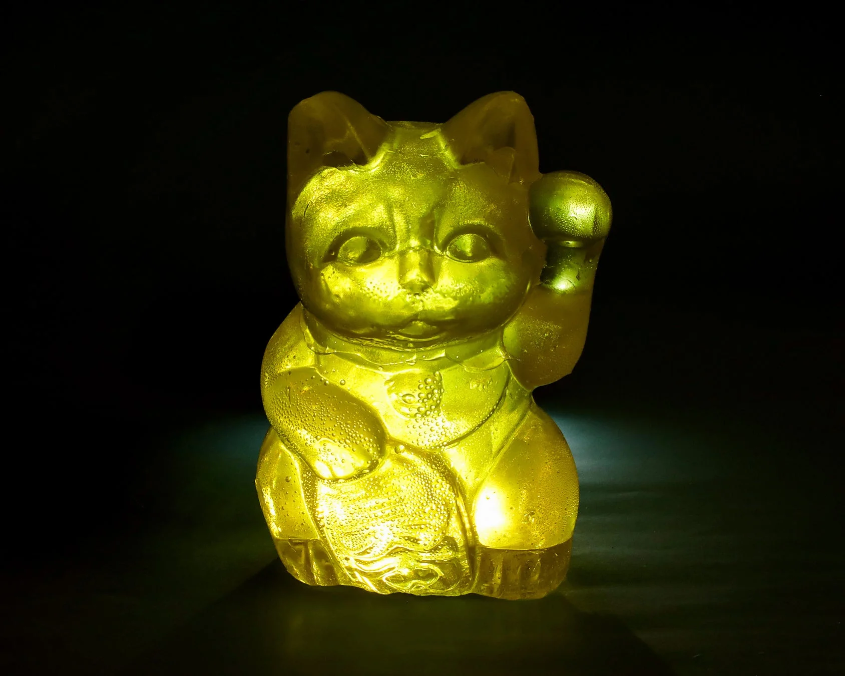 暗闇の中で明るく黄色く光る招き猫の置物。