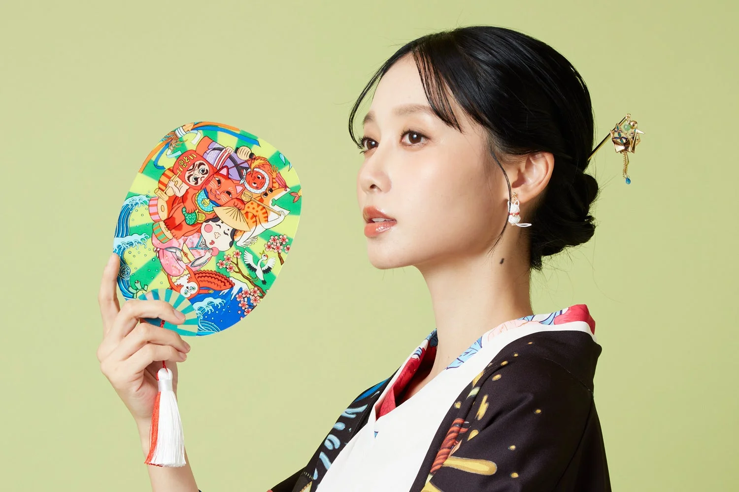 着物を着た女性が縁起物の絵柄が描かれた団扇を持っているポートレート