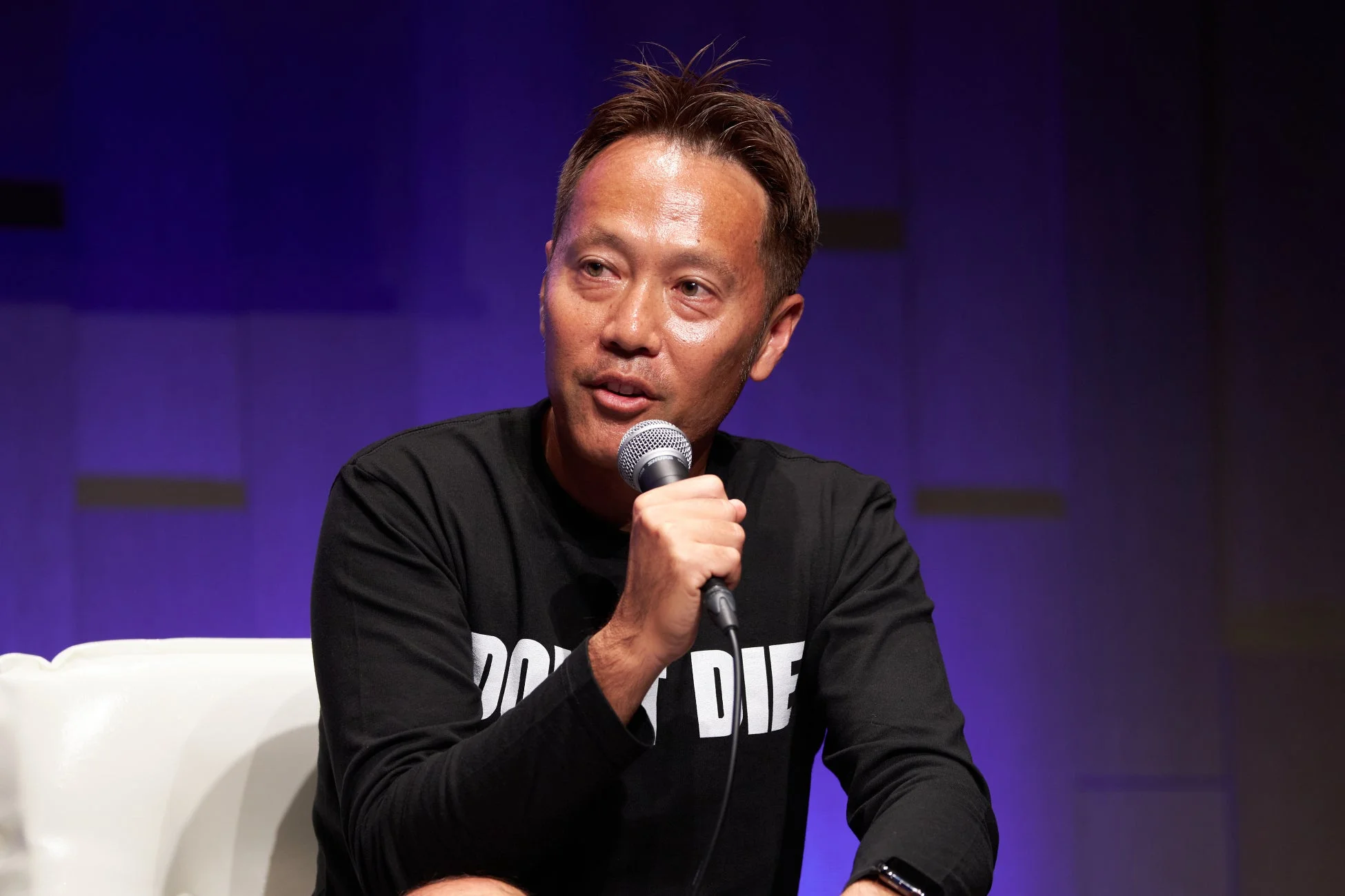 黒い長袖シャツを着た男性がマイクを持って話している様子