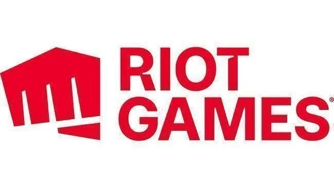 赤色の「RIOT GAMES」の文字と、左側に拳をモチーフにしたシンボルが特徴的な、ゲーム開発会社ライアットゲームズのロゴマーク