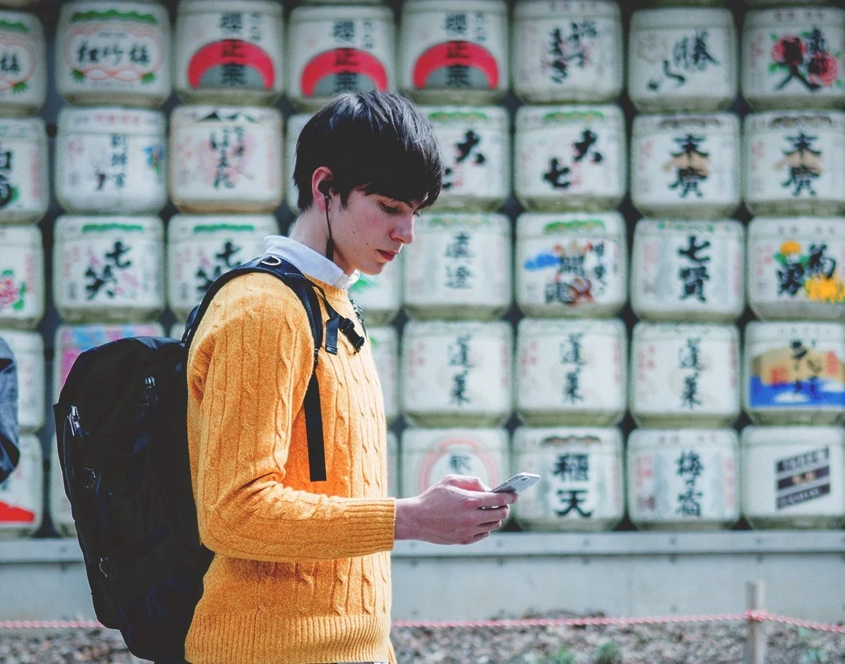 日本の伝統的な酒樽が積み重ねられた壁の前でスマートフォンを見ている若い男性