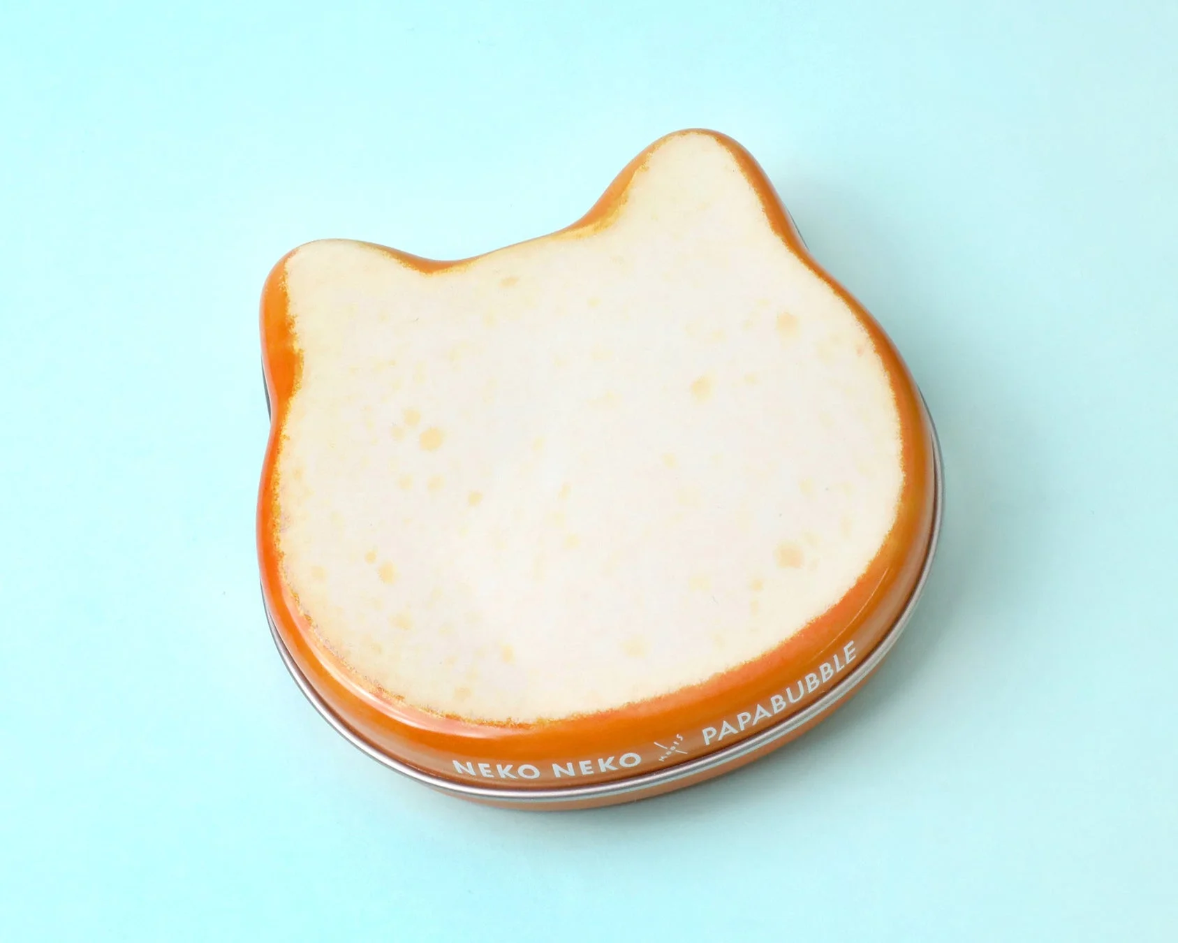 水色の背景に置かれた、猫の顔の形をした可愛らしいオレンジ色の缶です。