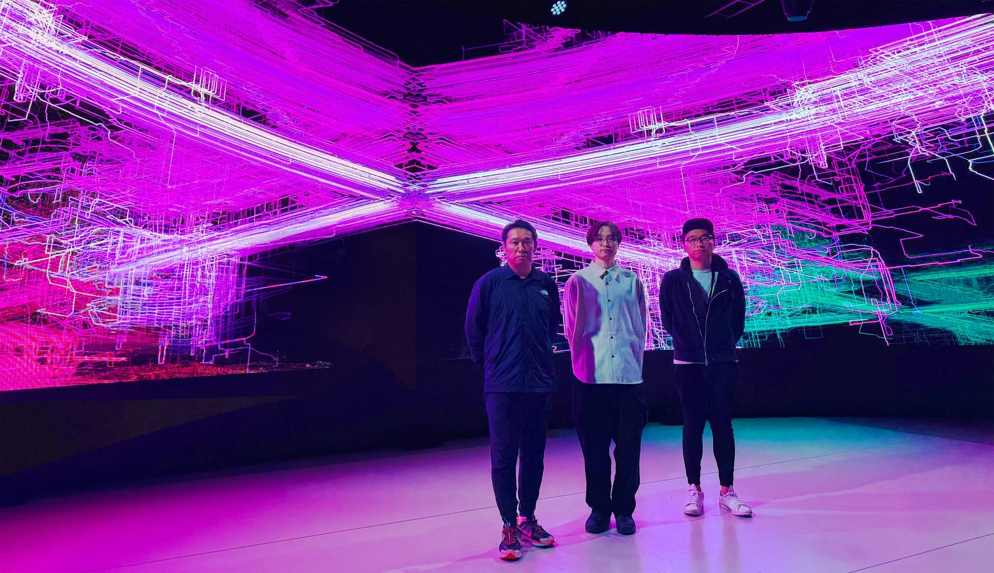 未来的なデジタルアートが映し出されたステージに立つ3人の男性