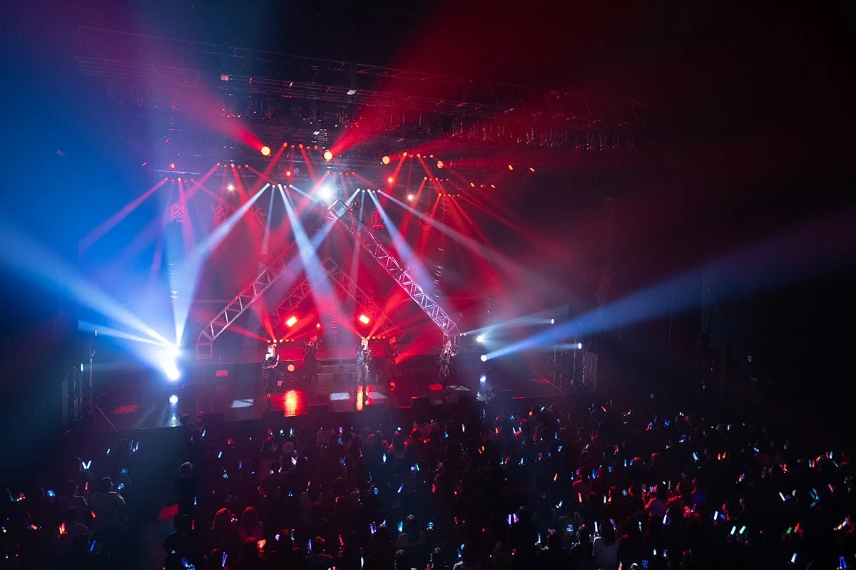 赤と青の鮮やかな照明が照らすステージでパフォーマーが熱演するライブコンサートの様子