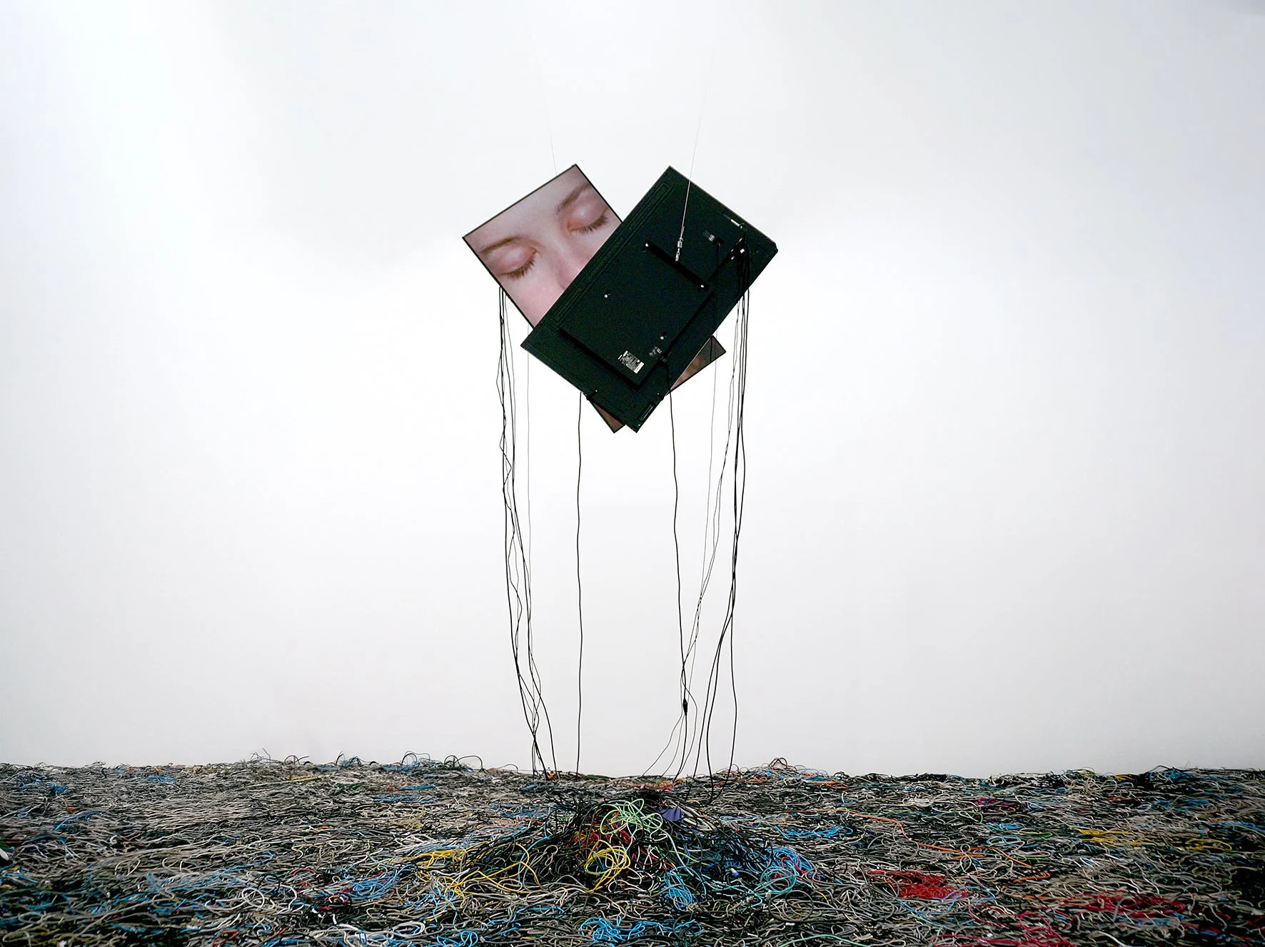 閉じた目が映るディスプレイと絡み合うケーブルのインスタレーション