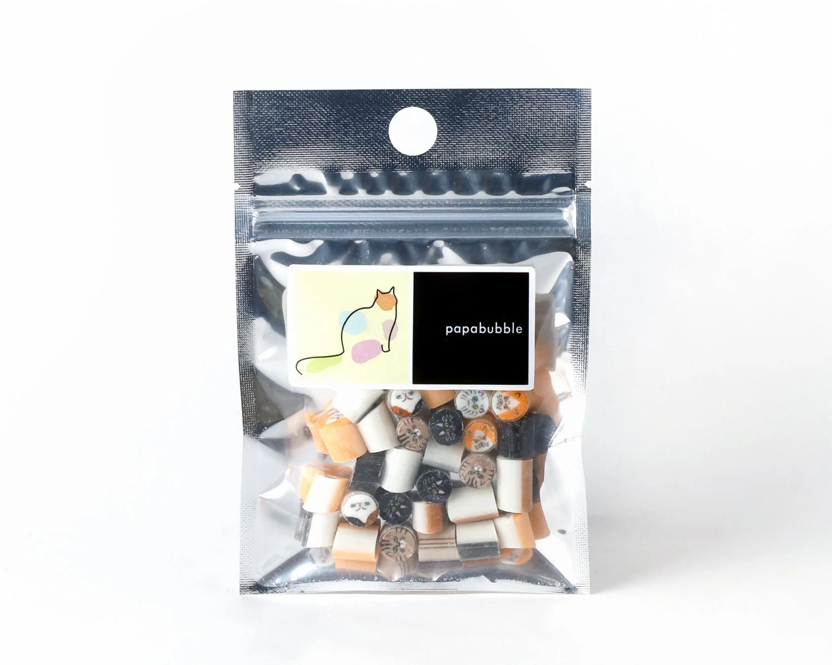 白い背景に置かれた、猫の顔がデザインされたカラフルなキャンディが詰まった銀色の袋です。papabubbleのロゴと猫のイラストが描かれたラベルが貼られています。