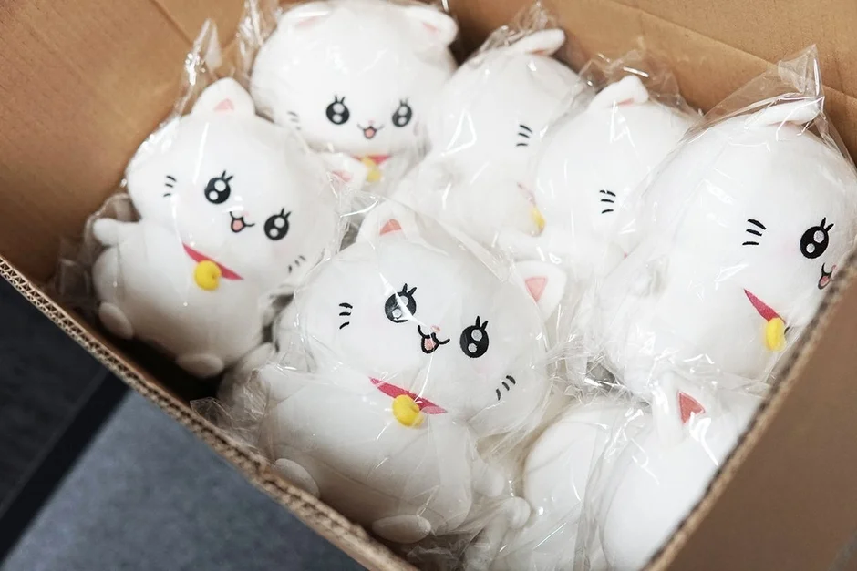 段ボール箱に、それぞれビニール袋に個包装された白い猫のぬいぐるみがたくさん詰まっている様子です。