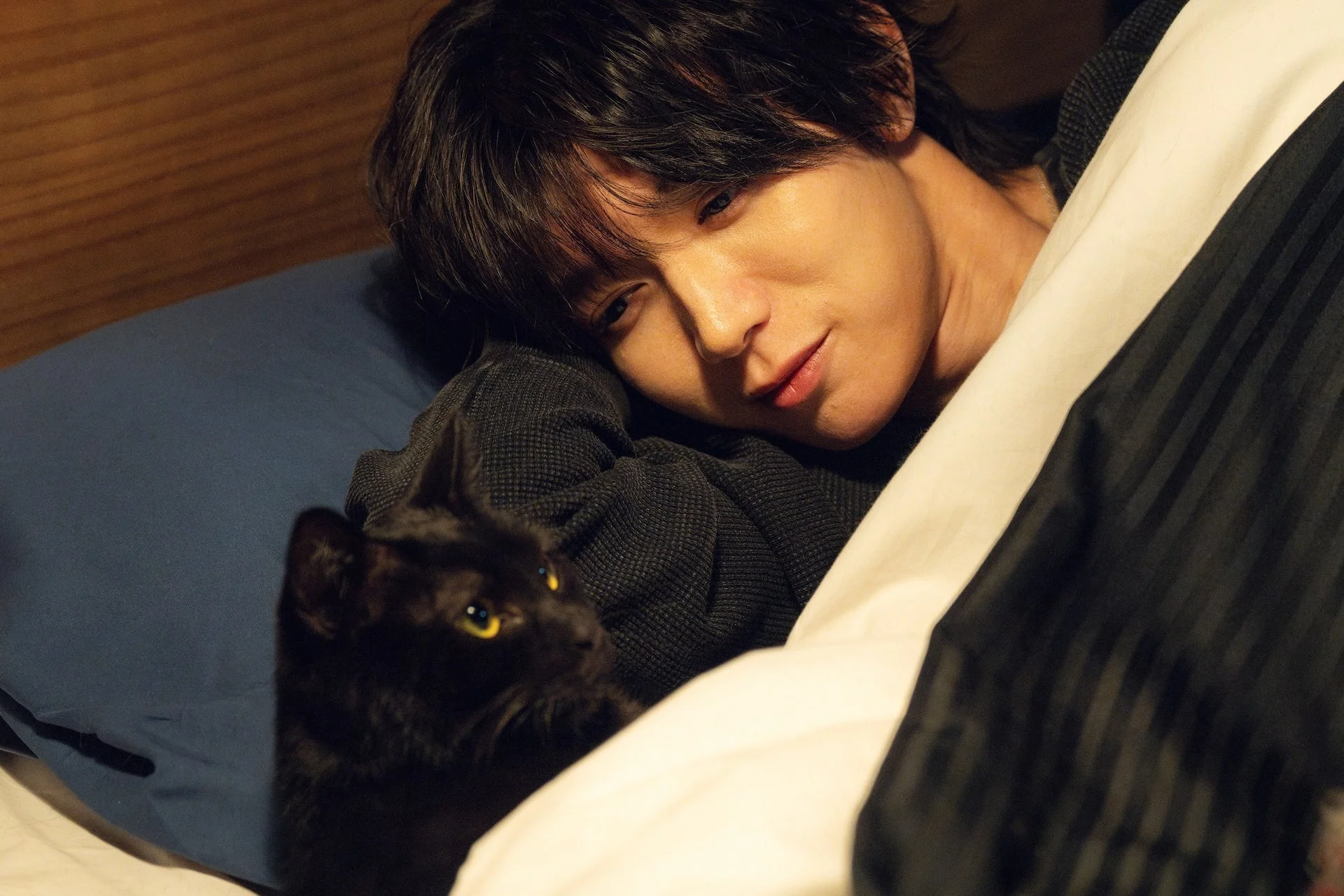 ベッドで黒猫とくつろぐ男性