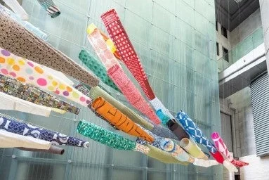建物のガラス壁面に飾られたカラフルな鯉のぼりのアートインスタレーション