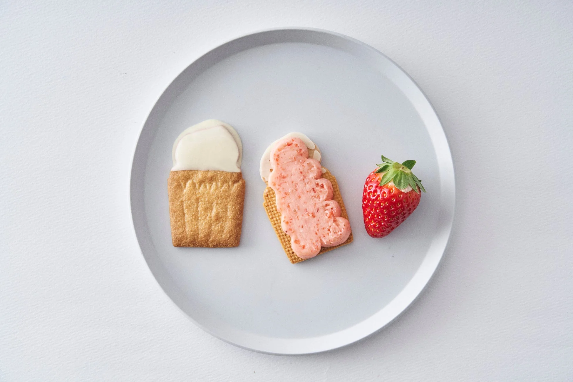 白い皿に、アイスクリームの形をした2つのクッキーと、鮮やかな赤いイチゴ