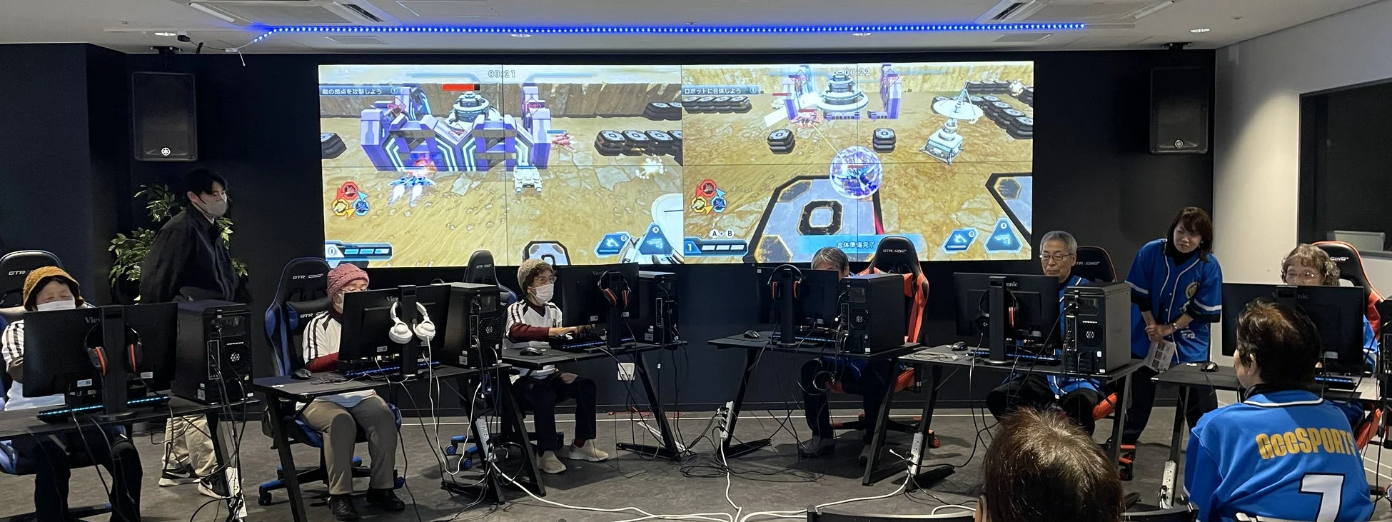 複数の高齢者がゲーミングチェアに座り、PCモニターに向かって真剣にゲームをプレイしている様子