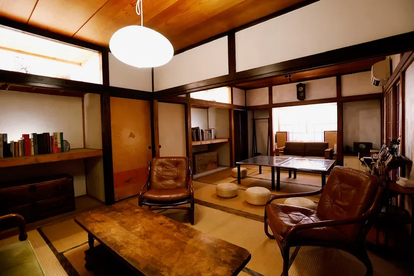 和と洋が融合した趣のあるリビングルーム。畳敷きの床に革張りのアームチェアや木製のテーブルが配置され、書棚には本が並んでいます。レトロな雰囲気と落ち着きが感じられる空間です。