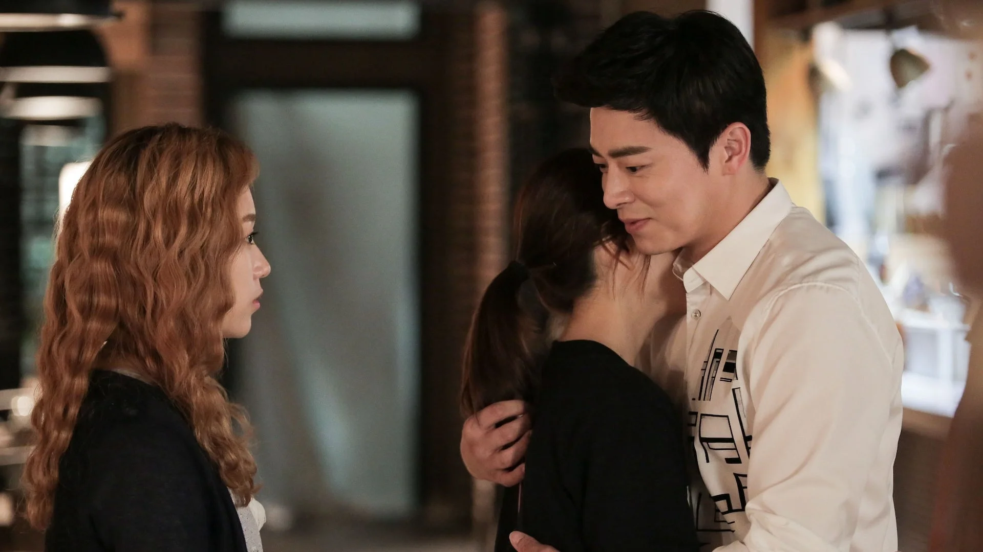 男性に抱きしめられる女性と、それを見つめる別の女性