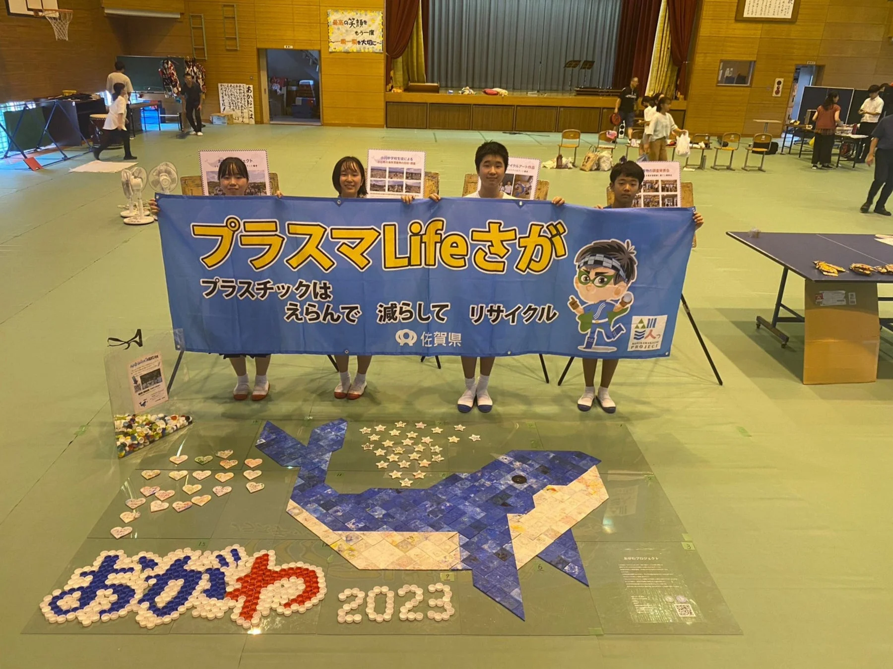 体育館で海洋プラスチックアート作品を囲む人々